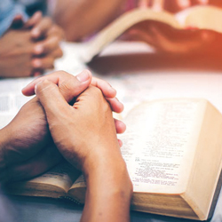 Group of hands praying over Bibles